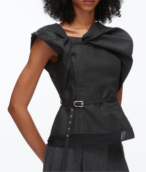A woman wears the 3.1 Phillip Lim Sleeveless Draped Bow Top w Belt, featuring an oversized shoulder detail and belted waist, paired with grey Italian ottoman weave trousers.