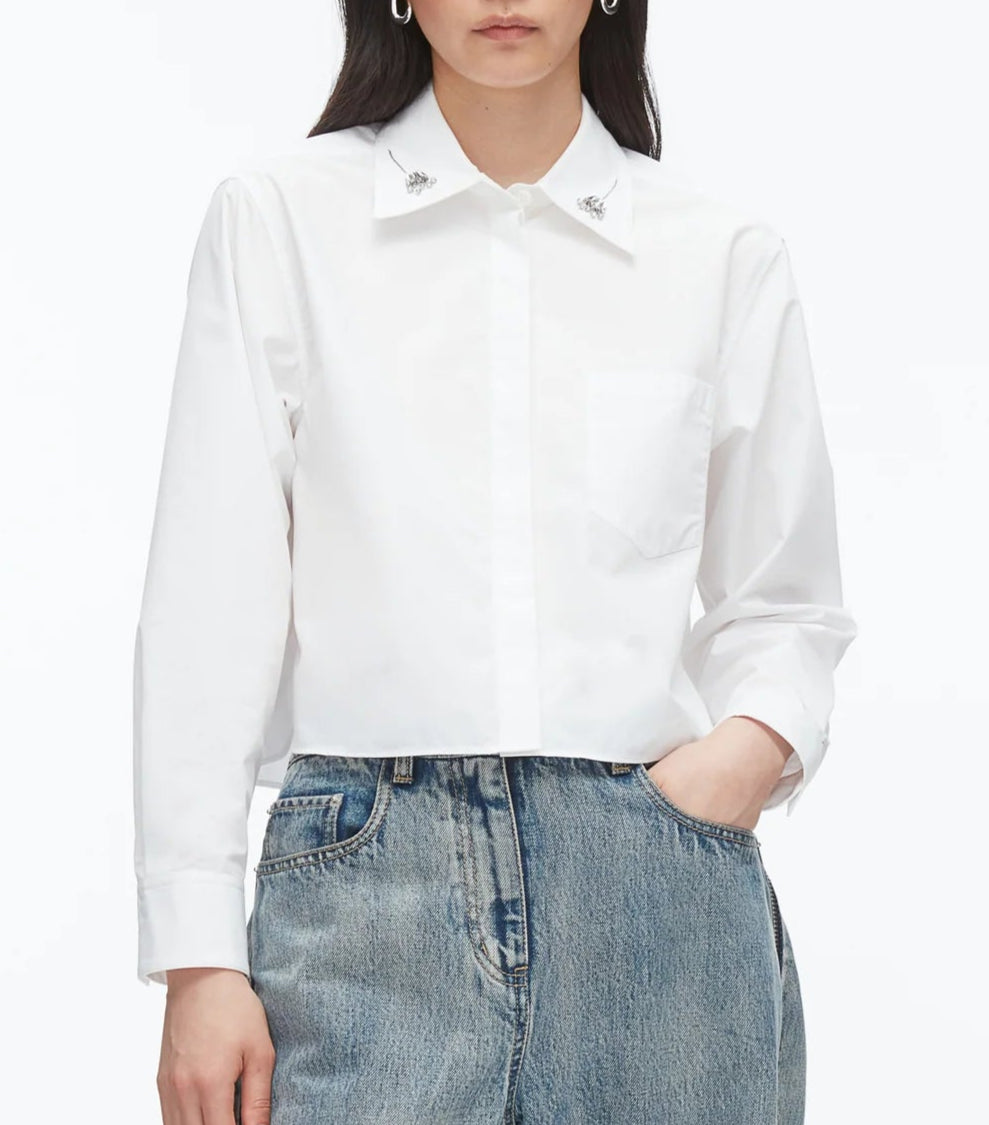 Wearing the 3.1 Phillip Lim Cropped Shirt with Embroidered Collar and light blue high-waisted jeans, this person stands with one hand in their pocket.