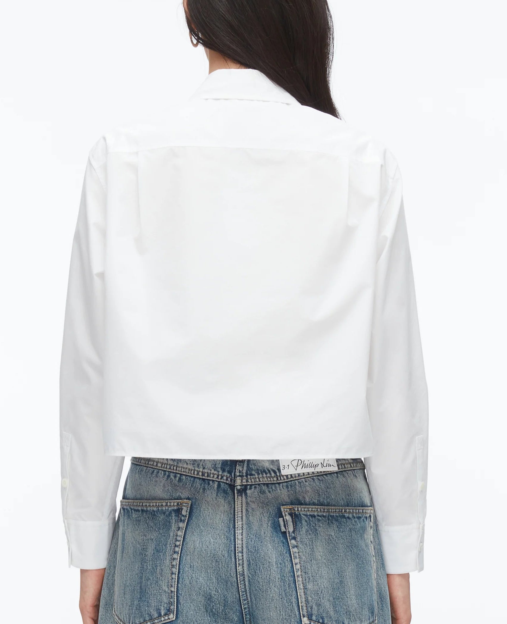 A person is seen from the back wearing a 3.1 Phillip Lim Cropped Shirt with Embroidered Collar, styled with high-waisted blue jeans against a plain background.