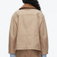 A person with long curly hair is seen from behind, wearing the 3.1 Phillip Lim Cropped Flounce Barn Jacket over a blue checkered shirt and tan pants against a plain white background.