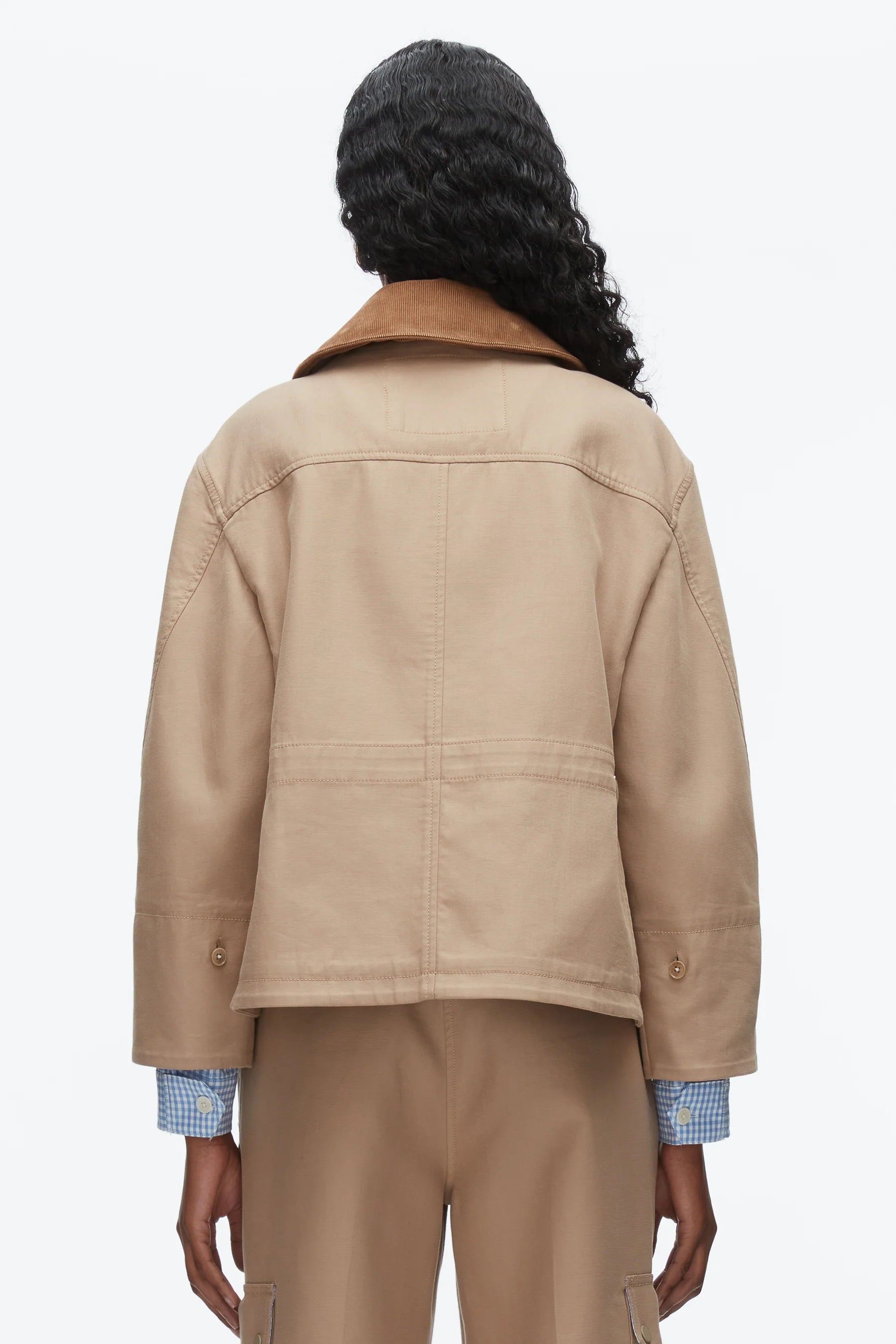 A person with long curly hair is seen from behind, wearing the 3.1 Phillip Lim Cropped Flounce Barn Jacket over a blue checkered shirt and tan pants against a plain white background.