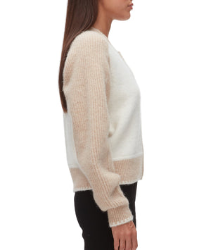 A woman stands in profile against a white background, wearing the 3.1 Phillip Lim Raglan Zip Cardigan in cream and beige with ribbed sleeves, paired with black pants.