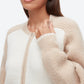 A woman wears the 3.1 Phillip Lim Raglan Zip Cardigan in beige and white, featuring ribbed sleeves, paired with gold hoop earrings. Shown from the shoulders up.