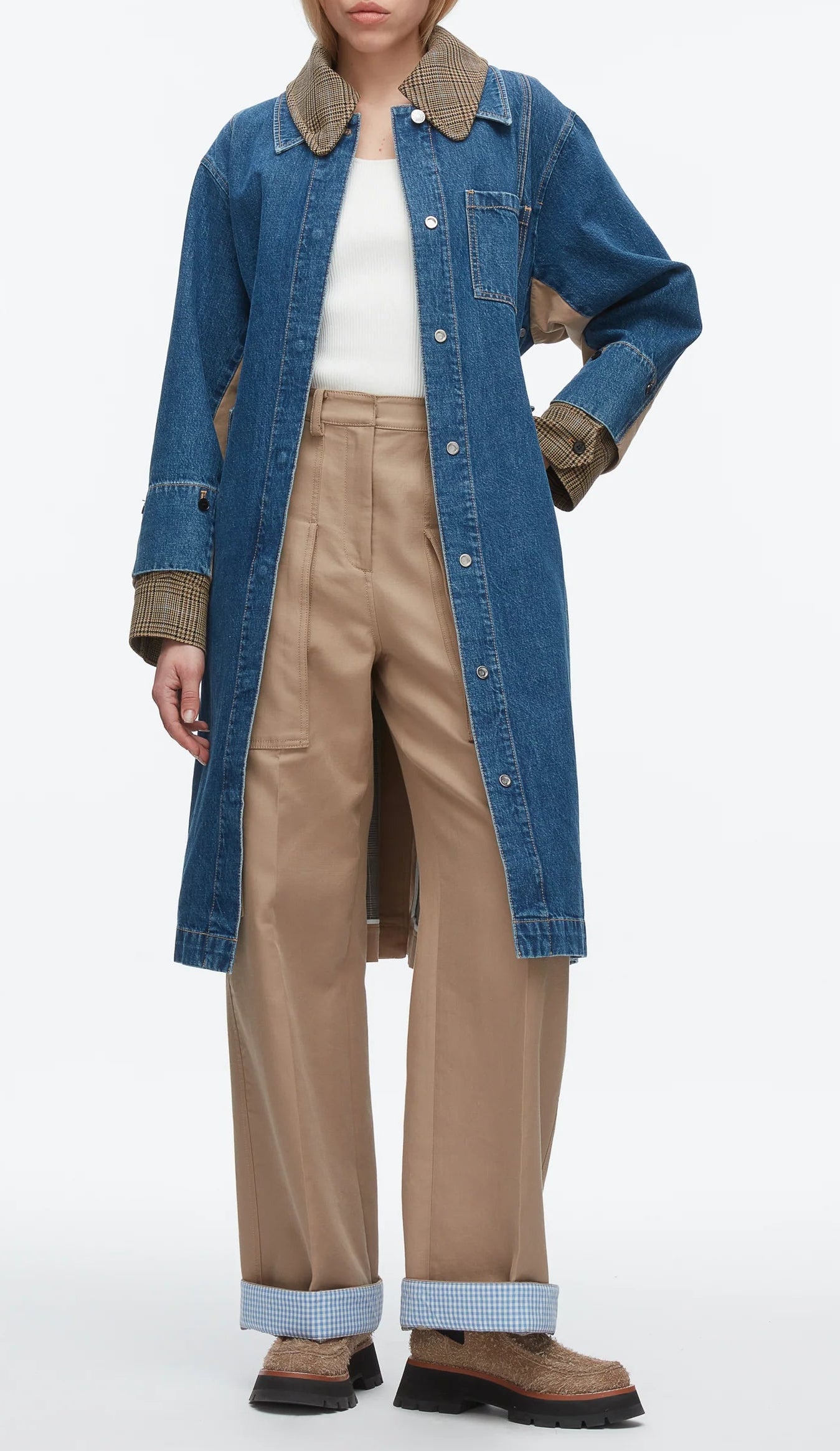 A person wears the 3.1 Phillip Lim Denim Combo Trench over a white top, paired with beige high-waisted pants with rolled cuffs and brown shoes.