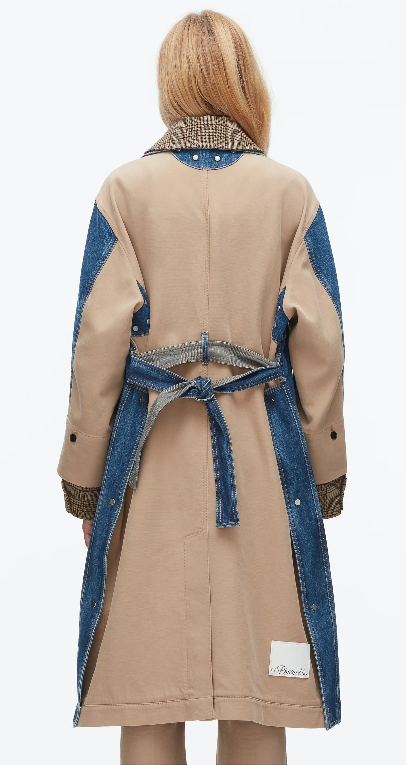 A person with long blonde hair is seen from behind wearing the 3.1 Phillip Lim Denim Combo Trench, featuring blue denim accents, a removable waist-cinching belt, and a checkered collar in a mixed-media design.