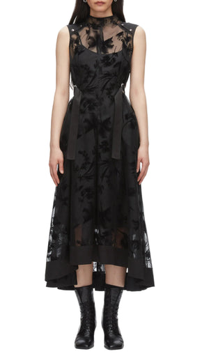 A woman in the 3.1 Phillip Lim Flocked Organza Sleeveless Midi Dress Combo, featuring a belted waist and sheer floral overlay, pairs it with black lace-up ankle boots for a modern occasion look against a white background.