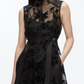 A woman wears the 3.1 Phillip Lim Flocked Organza Sleeveless Midi Dress Combo—featuring sheer black floral organza, a high neck, silver snap shoulder details, and a belted waist—for stylish modern occasions.