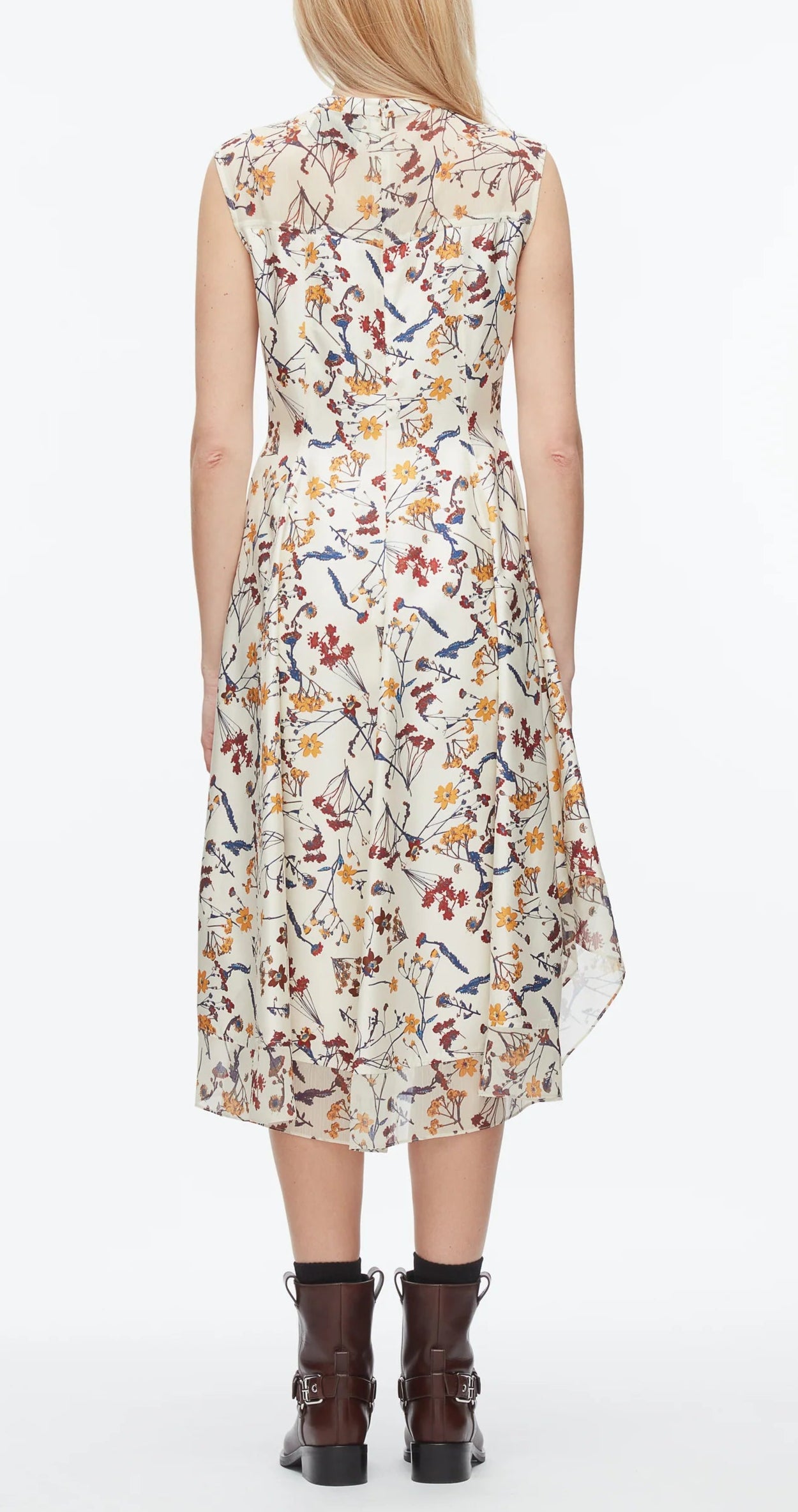 A woman faces away, wearing the 3.1 Phillip Lim Bliss Floral Sleeveless Dress with a chiffon hem, styled with brown ankle boots.