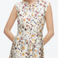 Woman in the 3.1 Phillip Lim Bliss Floral Sleeveless Dress Chiffon Hem, featuring a wildflower motif in red, yellow, and blue tones, stands with hands in pockets.