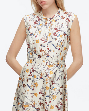 Woman in the 3.1 Phillip Lim Bliss Floral Sleeveless Dress Chiffon Hem, featuring a wildflower motif in red, yellow, and blue tones, stands with hands in pockets.