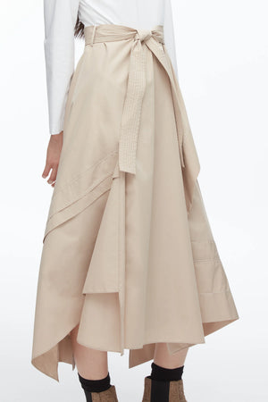 A person wearing the 3.1 Phillip Lim Combo T-Shirt Dress, featuring a beige cotton poplin skirt with asymmetric draping and a tied waist belt, paired with a white long-sleeve top.