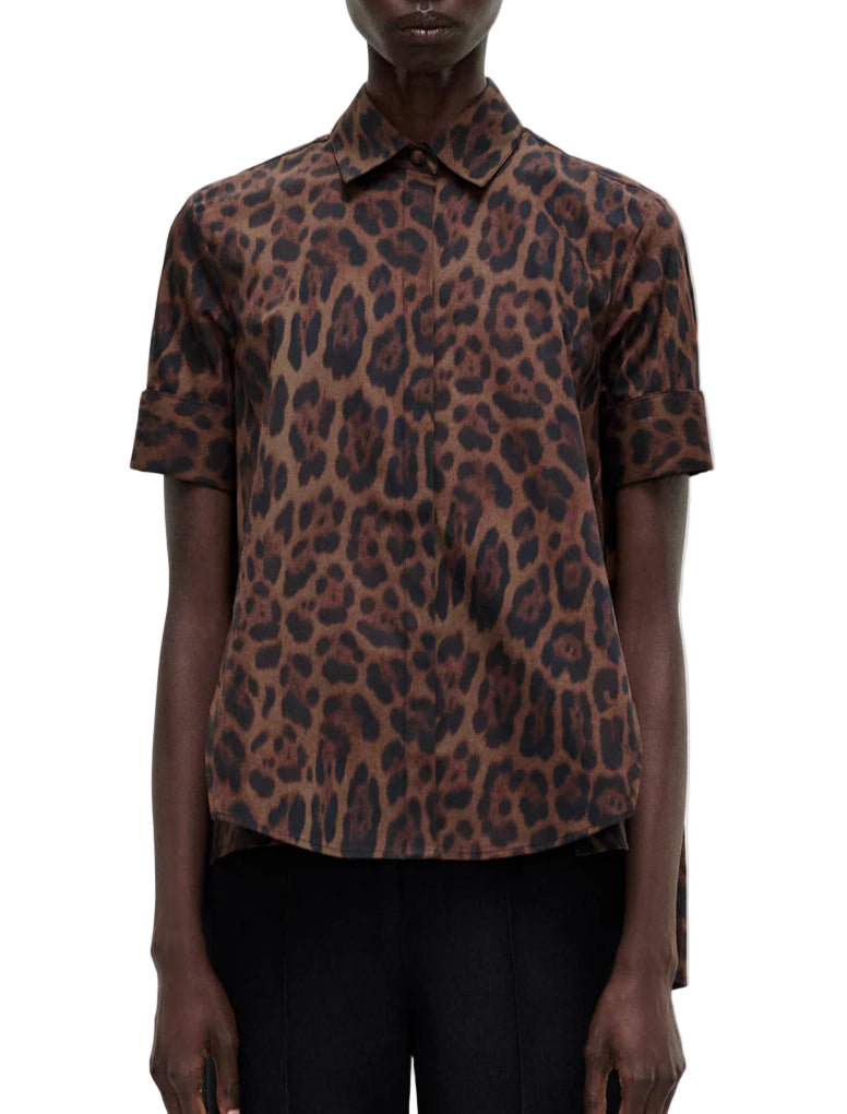 A model wears the Adam Lippes Trapeze Shirt Printed Poplin Leopard—a short-sleeve, collared top in brown and black leopard print cotton poplin—paired with black pants, front view against a white background.