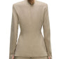 A person faces away from the camera, wearing the Adam Lippes Noa Top—a beige tailored blazer with removable shoulder pads—paired with matching trousers, set against a white background.