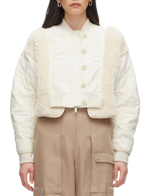 A person models the 3.1 Phillip Lim Cropped Sherpa Combo Bomber with beige cargo pants. Their long, dark hair flows freely as they face forward, effortlessly showcasing this stylish quilted jacket with faux shearling trim.