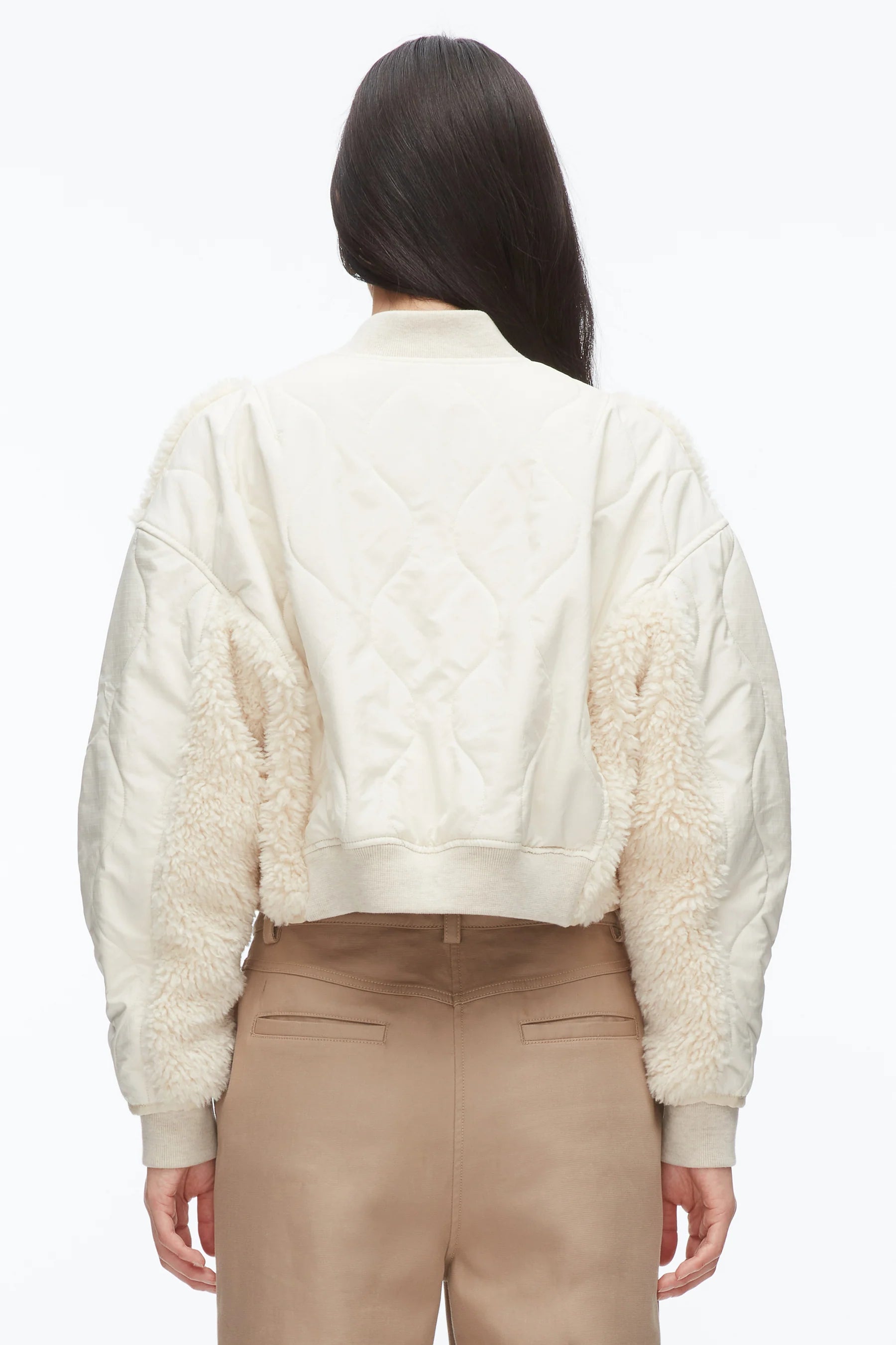 Person stands with their back to the camera, wearing the 3.1 Phillip Lim Cropped Sherpa Combo Bomber in cream and beige pants against a plain background.