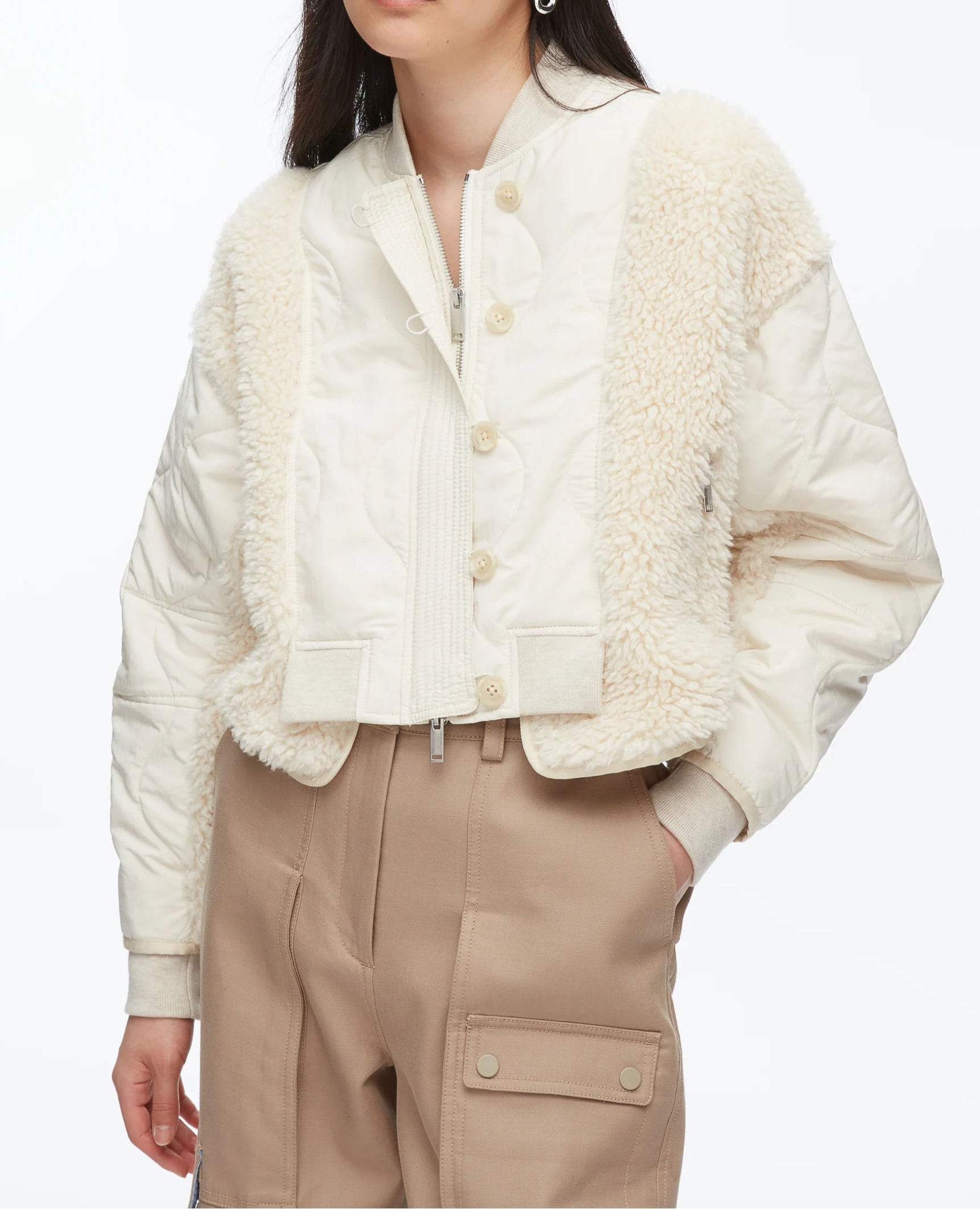 A woman wears the 3.1 Phillip Lim Cropped Sherpa Combo Bomber over a white top and high-waisted beige cargo pants.