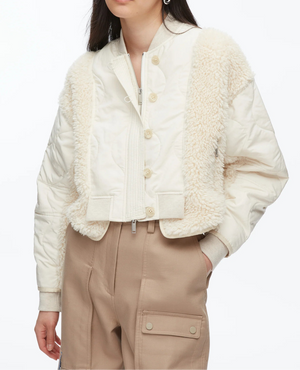 A woman wears the 3.1 Phillip Lim Cropped Sherpa Combo Bomber over a white top and high-waisted beige cargo pants.