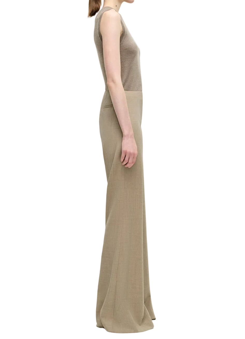 A person in profile wears the Adam Lippes Lamy Pant—a high-waisted, flared silhouette in beige Italian tropical wool—paired with a sleeveless taupe top, set against a white background.