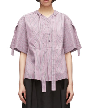 A person is wearing the 3.1 Phillip Lim Short Sleeve Striped Tie Neck Blouse, featuring light purple pinstripes, a V-neck placket with button front, tie details, and a relaxed silhouette, paired with a black skirt and standing against a white background.