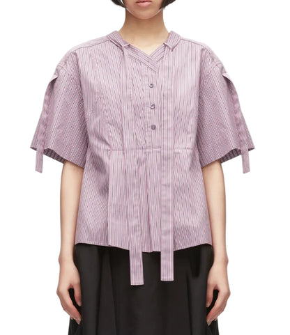 A person is wearing the 3.1 Phillip Lim Short Sleeve Striped Tie Neck Blouse, featuring light purple pinstripes, a V-neck placket with button front, tie details, and a relaxed silhouette, paired with a black skirt and standing against a white background.