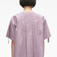A person with short dark hair is seen from the back against a plain white background, wearing the 3.1 Phillip Lim Short Sleeve Striped Tie Neck Blouse—a loose-fitting, purple and white striped top with a relaxed silhouette.