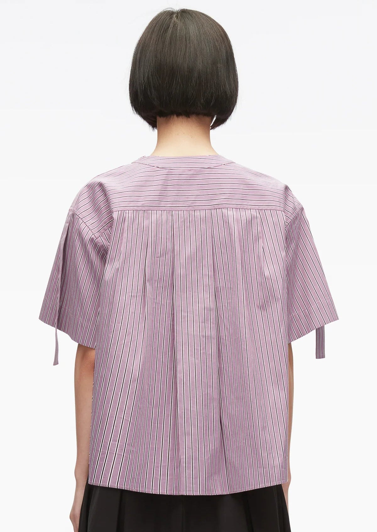 A person with short dark hair is seen from the back against a plain white background, wearing the 3.1 Phillip Lim Short Sleeve Striped Tie Neck Blouse—a loose-fitting, purple and white striped top with a relaxed silhouette.