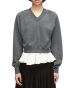 A person facing forward wears the 3.1 Phillip Lim Ultrafine Merino V Neck Pullover in grey, featuring a white pleated ruffle detail at the hem, paired with a black skirt.