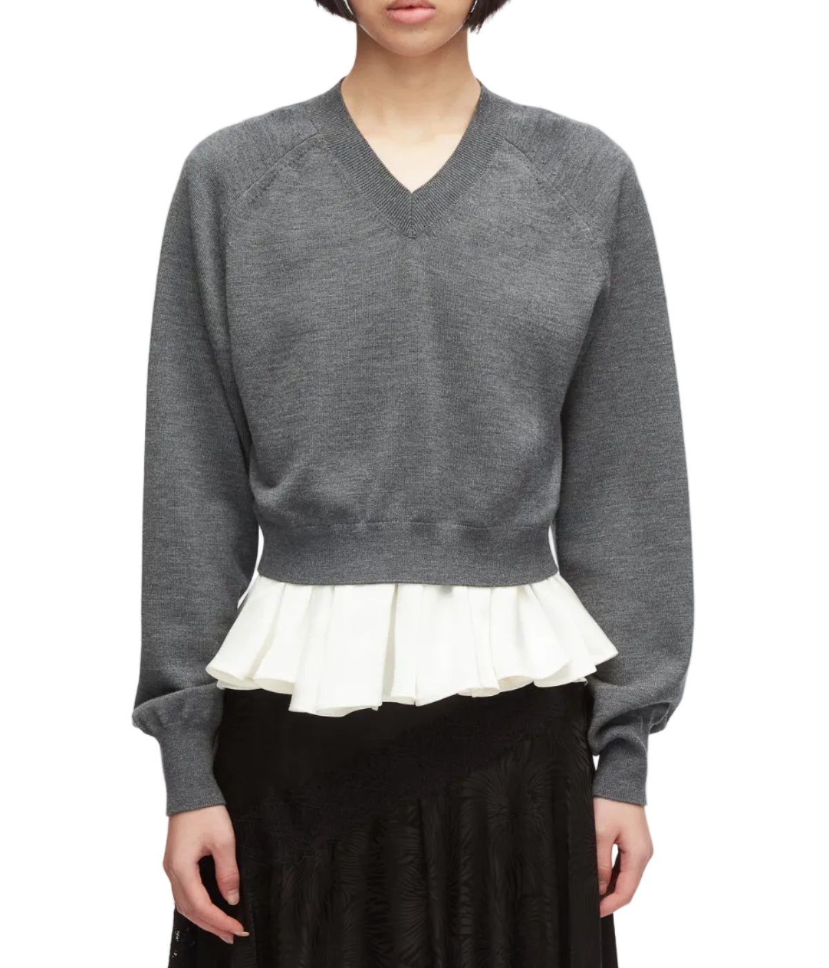 A person facing forward wears the 3.1 Phillip Lim Ultrafine Merino V Neck Pullover in grey, featuring a white pleated ruffle detail at the hem, paired with a black skirt.