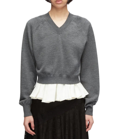 A person facing forward wears the 3.1 Phillip Lim Ultrafine Merino V Neck Pullover in grey, featuring a white pleated ruffle detail at the hem, paired with a black skirt.