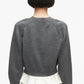 A person with short dark hair, seen from behind, wears the 3.1 Phillip Lim Ultrafine Merino V Neck Pullover in gray, layered over a white pleated top and a dark skirt, against a plain white background.