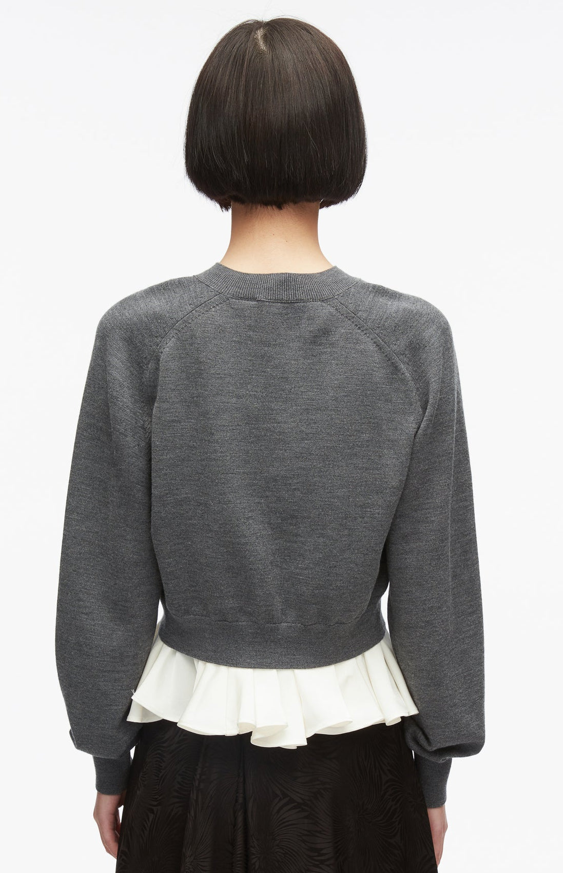 A person with short dark hair, seen from behind, wears the 3.1 Phillip Lim Ultrafine Merino V Neck Pullover in gray, layered over a white pleated top and a dark skirt, against a plain white background.