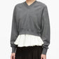 A woman wearing the 3.1 Phillip Lim Ultrafine Merino V Neck Pullover in grey, styled over a white ruffled blouse and paired with a black skirt, stands against a plain white background.
