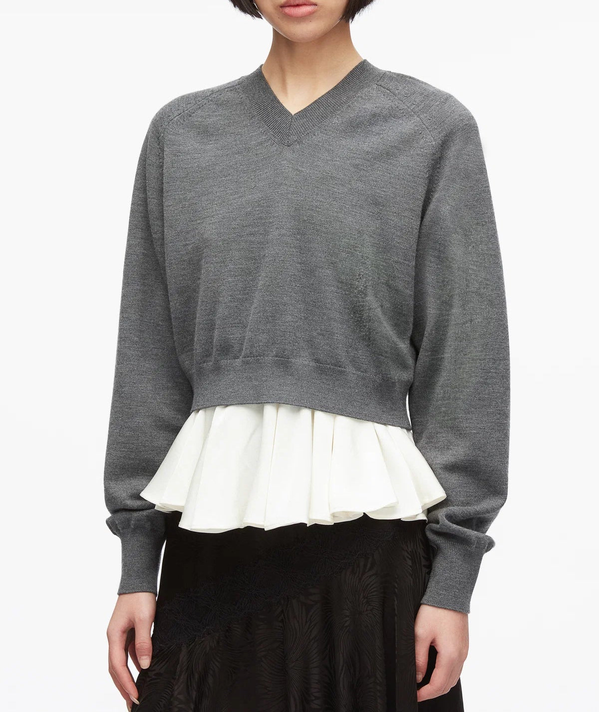 A woman wearing the 3.1 Phillip Lim Ultrafine Merino V Neck Pullover in grey, styled over a white ruffled blouse and paired with a black skirt, stands against a plain white background.