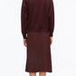 A person stands facing away, wearing the Ultrafine Merino Polo Midi Dress by 3.1 Phillip Lim in burgundy, paired with black socks and black shoes, against a plain white background.