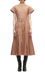 A woman stands against a white background wearing the 3.1 Phillip Lim Pleated Poplin Tulip Sleeves Midi Dress in light brown, featuring short tulip sleeves, pintuck detailing, a self-tie belt, and a pleated skirt, paired with black knee-high boots.