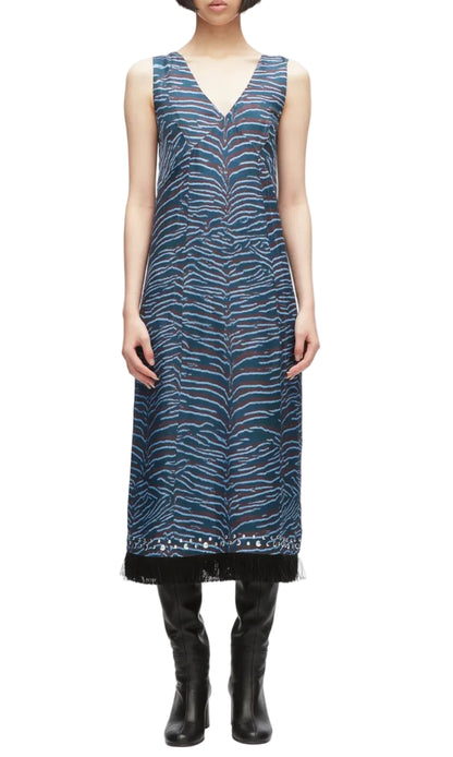 A woman wears the Tiger Print Studded Midi Dress by 3.1 Phillip Lim, a sleeveless blue midi dress featuring an abstract tiger motif and V-neckline, paired with black boots and set against a white background.