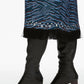 A person wearing the 3.1 Phillip Lim Tiger Print Studded Midi Dress, featuring a blue pattern with a fringed hem and silver studs, paired with black knee-high heeled leather boots.
