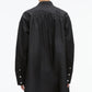 A person wearing the 3.1 Phillip Lim Long Sleeve Poplin Mini Dress, featuring a loose-fitting black silhouette with gathered detailing, is shown from the back with hair in a bun and silver hoop earrings.