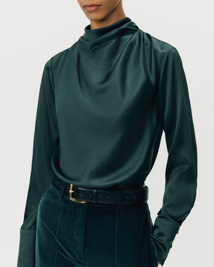 Model in the Adam Lippes Blaine Silk Cashmere Top in hunter green, styled with dark high-waisted pants and a black belt featuring a gold buckle.