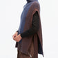 A person wears the 3.1 Phillip Lim Bicolor Rib Funnel Neck Vest—a sleeveless, oversized knit in painterly blue and brown alpaca blend—layered over a black shirt and brown zippered pants, standing against a white background.