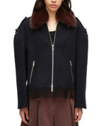 A woman wearing the 3.1 Phillip Lim Wool Blanket Zip Up Jacket, featuring a navy virgin wool construction with a faux fur collar, zippered pockets, and fringe detailing at the hem, styled over a brown skirt.