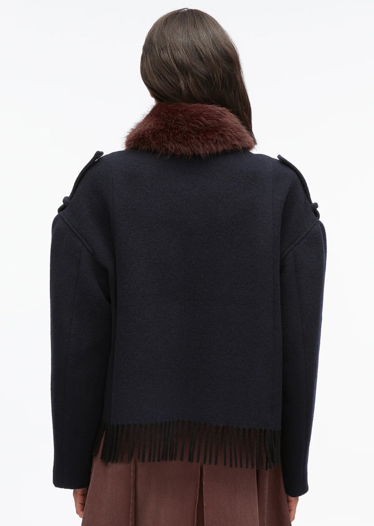 Person with long brown hair wearing the 3.1 Phillip Lim Wool Blanket Zip Up Jacket—an artisanal outerwear piece featuring a dark hue, faux fur collar, and fringe hem—photographed from behind against a plain background.