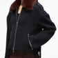 A person wears the 3.1 Phillip Lim Wool Blanket Zip Up Jacket—a dark handcrafted outerwear piece featuring a brown faux fur collar and fringe at the hem—paired with brown pants.