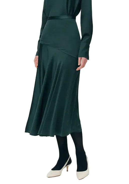 Model wearing the Tess Silk Charmeuse Skirt by Adam Lippes with a matching green top, black tights, and white low heels, posed against a white background.
