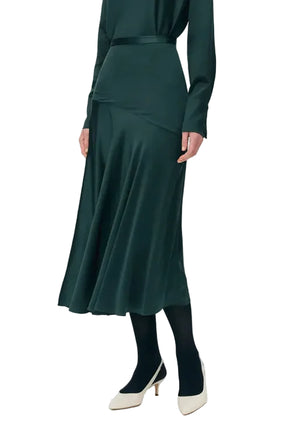 Model wearing the Tess Silk Charmeuse Skirt by Adam Lippes with a matching green top, black tights, and white low heels, posed against a white background.