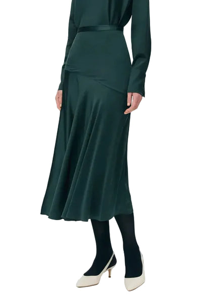 Model wearing the Tess Silk Charmeuse Skirt by Adam Lippes with a matching green top, black tights, and white low heels, posed against a white background.