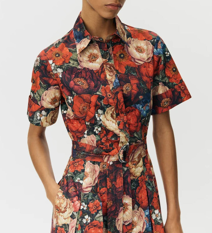 Person wearing the Leighton Dress by Adam Lippes, in Italian cotton poplin with a bold red, orange, and cream floral print and belted waist, against a plain background.