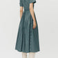 Woman with back turned wears the Doron Stripe Shirting Dress by Adam Lippes and knee-high white heeled boots against a plain background.
