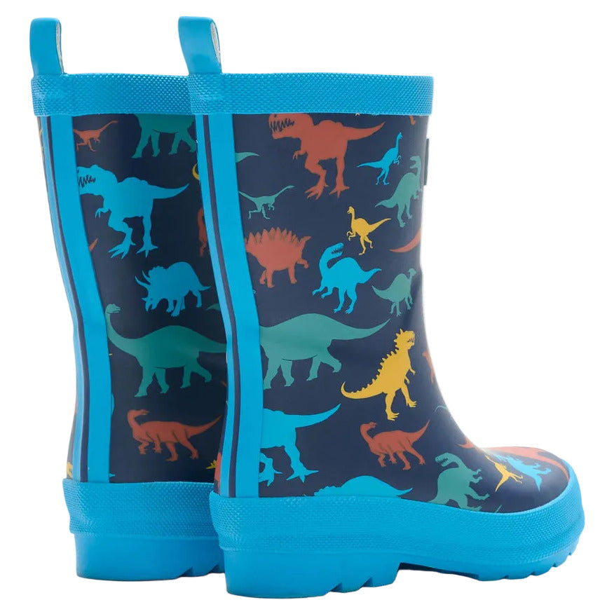 Hatley Boys’ Colourful Dinos Matte Rain Boots, featuring blue soles and a vibrant multicolored dinosaur print on a dark background, are shown from the back and side angles—perfectly waterproof for rainy-day adventures.