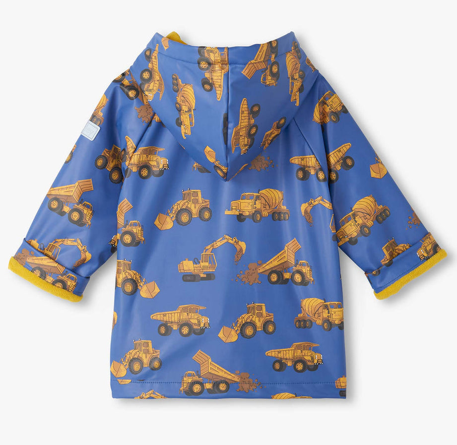 Hatley’s Baby Boys’ and Boys’ Construction Trucks Rain Coat is a vibrant blue hooded rain jacket for kids, decorated with bright yellow prints of dump trucks, excavators, and cement mixers. Shown laid flat with the sleeves and hood visible, this waterproof jacket is perfect for keeping little ones dry on rainy days.